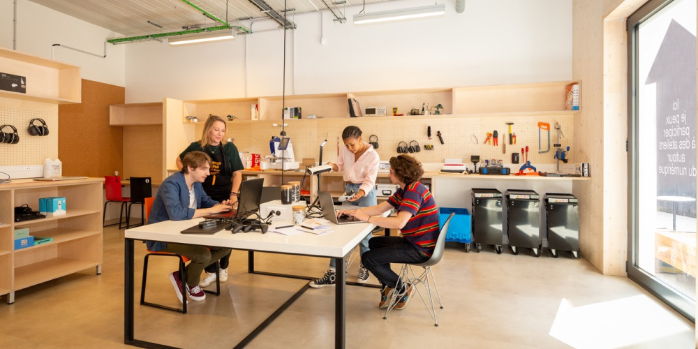 Trois étudiants accompagnés d’une professeure travaillent sur des ordinateurs et des manettes de jeux vidéo.