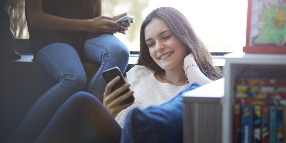 Une jeune femme regarde son téléphone en souriant.