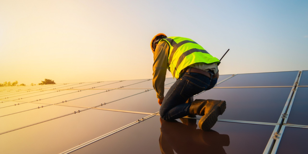A worker works on a roof during the sunset. 