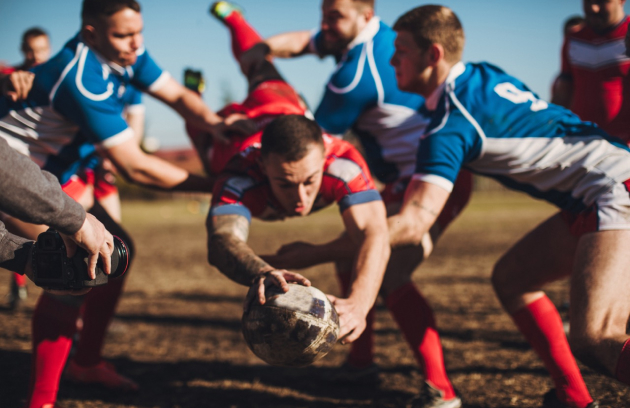 Un joueur de rugby se lance en avant pour marquer un essai entouré de ses adversaires.