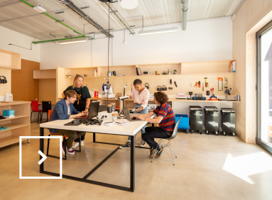 Trois étudiants accompagnés d’une professeure travaillent sur des ordinateurs et des manettes de jeux vidéo.