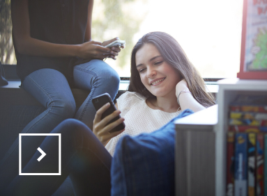 Une jeune femme dans un parc regarde son téléphone en souriant.