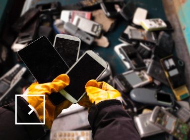 Une personne avec des gants orange trie de dizaines de téléphones mobiles.